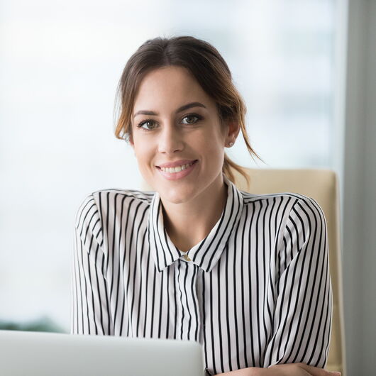 Frau sitzt im Büro am Laptop und lächelt