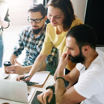 Ein Team sitzt zusammen an einem Laptop und erabeitet etwas