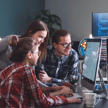 Drei Personen sitzen im Büro vor einem Computer